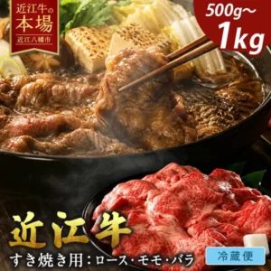 すき焼き鍋で箸が牛肉をつまみ上げ、焼き豆腐・白菜・しいたけ・ねぎ・春菊などが入った様子と、手前の皿にのせた生の牛肉の薄切りを写した、近江牛 ロース・モモ・バラ すき焼き用の商品写真。店舗が画像に入れた表示「近江牛の本場」「近江八幡市」「500g〜1kg」「近江牛」「すき焼き用：ロース・モモ・バラ」「冷蔵便」