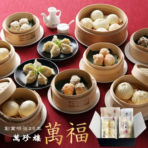 蒸籠と皿に盛った焼売・水餃子・肉まん・あんまんと、黒い箱に入ったギフトセットを赤い背景に並べた萬珍樓 萬福 点心詰合せ 6種34個の商品写真。店舗が画像に入れた表示「創業明治25年」「萬珍樓」「萬福」