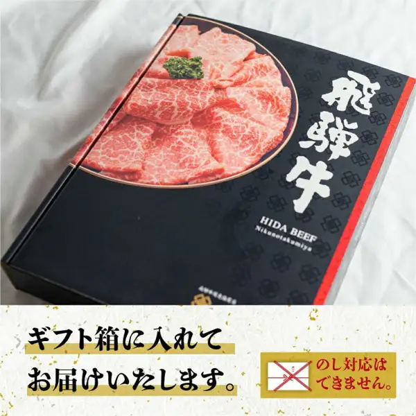 白い布の上に置かれた、霜降り肉の写真と緑の飾りが印刷され「飛騨牛」「HIDA BEEF」「Nikunotakumiya」の文字が入った黒と赤の箱が写る商品写真（肉の匠家 飛騨牛 肩ロース すき焼き・しゃぶしゃぶ用 500g）。店舗が画像に入れた表示として「ギフト箱に入れてお届けいたします。」「のし対応はできません。」の文字