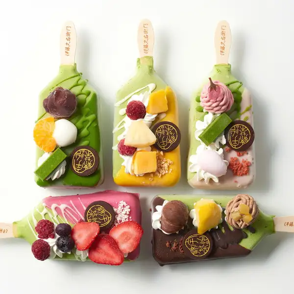 Product photo of five kinds of matcha parfait ice bars laid out on a white background, three on the top row and two on the bottom. The five are matcha, tropical, sakura, strawberry and marron, each with a round chocolate decoration bearing the shop's logo. Itohkyuemon Matcha Parfait Ice Bar, 5-Piece Set