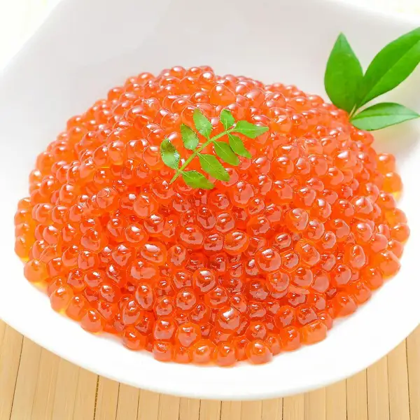 Serving-suggestion photo of soy-marinated salmon roe (ikura) heaped on a white plate with leaf garnishes at the center and upper right (soy-marinated ikura 500g, Hokkaido salmon roe, from 築地の王様). The image contains no text