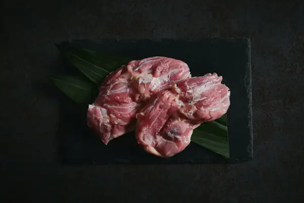 笹の葉を敷いた黒いスレートの上に、生の鶏もも肉を並べた、純系 名古屋コーチン モモ肉 1kg 朝引きの商品写真。画像内に文字の表示はありません。