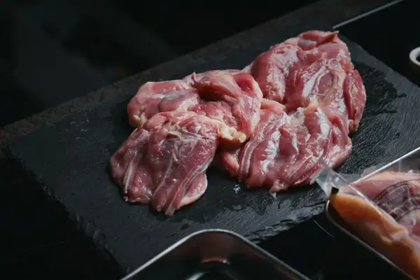 在黑色石板台上摆放着生鸡腿肉的商品照片,商品为纯系 名古屋コーチン 鸡腿肉 1kg 朝引き。右下方可见金属托盘。图片内没有文字。