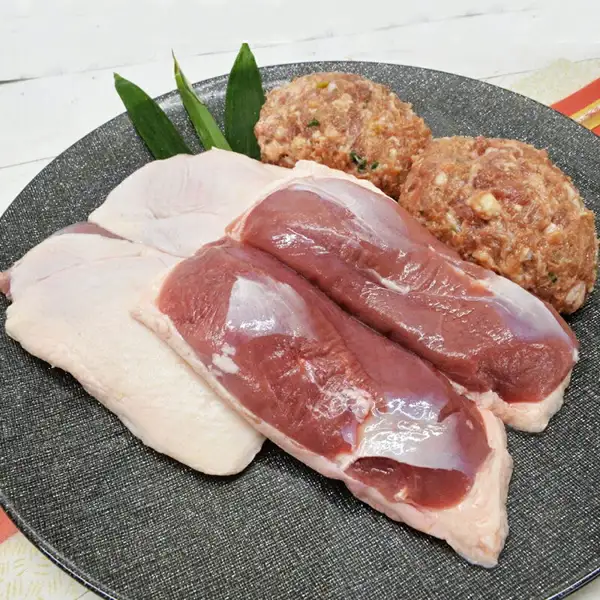 鴨鍋三昧セットの商品写真。皮付きの鴨肉と鴨つくね2個を、葉を添えた灰色の丸皿に並べた様子
