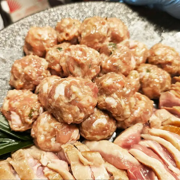 鴨鍋三昧セットの中身の写真。鴨つくねの山と、切り分けた皮付きの鴨肉を灰色の大皿に盛った様子