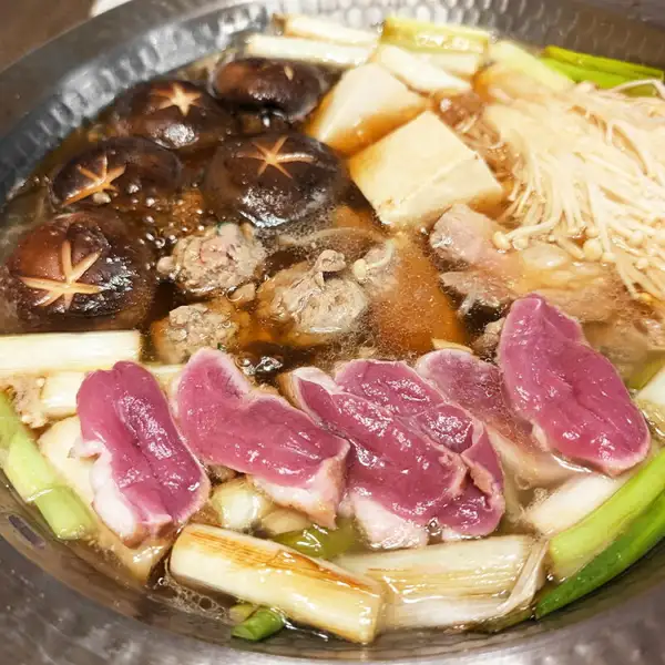 鴨鍋三昧セットの鍋料理の例。鴨肉と鴨つくねに、しいたけ・豆腐・えのきたけ・長ねぎを加えた鍋（盛り付け例）