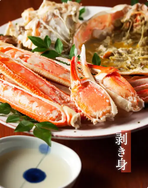 摆盘示例照片：白色大盘中放着取出壳的蟹腿肉和装在蟹壳里的蟹味噌，点缀绿叶，前方有一个盛着白色液体的小碗。店铺加在图片上的标示：「剥き身」（剥壳蟹肉）。