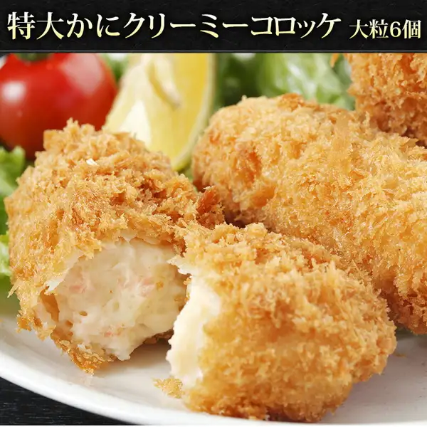 Product photo of Uoko Crab Cream Croquettes, 6 Large Pieces: several fried croquettes served on a plate, with the front one broken open to show the white cream filling. A lemon wedge, cherry tomato and lettuce are placed behind and to the left. Text the shop placed in the image: “特大かにクリーミーコロッケ 大粒6個” (extra-large crab creamy croquettes, 6 large pieces).