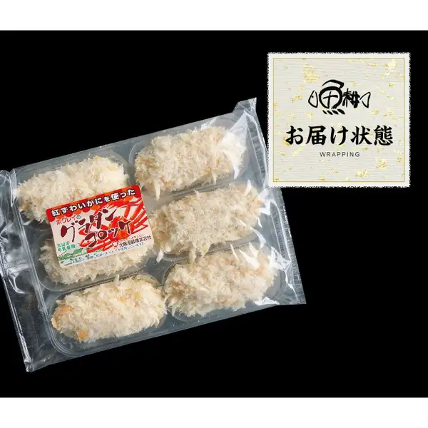 魚耕 カニクリームコロッケ 大粒6個のお届け状態の商品写真。黒い背景に、透明なトレー包装の中でパン粉の衣をつけたコロッケ6個が2列3段で並ぶ。包装のラベルには「紅ずわいがにを使った」「ホクレイの」「グラタンコロッケ」「大山の牛乳使用」と、小さな事業者名（判読できない）が印刷されている。右上に店舗ロゴと「お届け状態」「WRAPPING」の文字あり。
