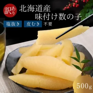黑色盘子里盛着黄色味付け数の子（鲱鱼子），一块被筷子夹起，右侧点缀绿叶的商品照片。图片中的文字：左上红色圆圈内「訳あり」，上方「北海道産 味付け数の子」(北海道产调味鲱鱼子)，其下「塩抜き」「皮むき」「不要」(无需脱盐、无需剥皮)，右下「500g」。（ましけマルシェ 味付け数の子 訳あり 折れ 500g）
