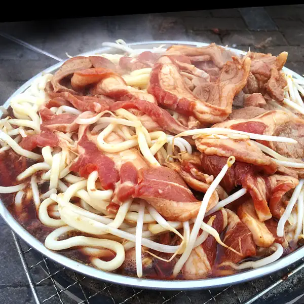 圆形铁板上放着羊肉、豆芽和乌冬面的烹调示例照片（味付きジンギスカン ラム肉 厚切 1kg）。豆芽和乌冬面不包含在商品中