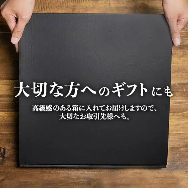 牛タン 訳あり 厚切り 1kgの商品ページの画像。木の台の上の黒い箱を、上部の左右から両手で支えている。箱の中央に店舗が画像に入れた表示「大切な方へのギフトにも」「高級感のある箱に入れてお届けしますので、大切なお取引先様へも。」の文字が入っている