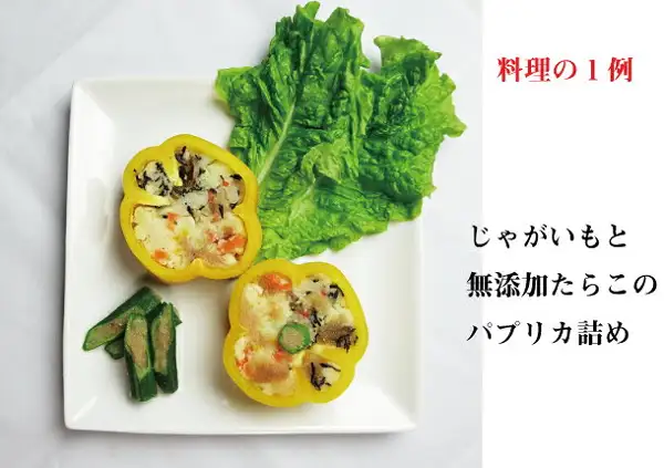 黄色いパプリカにじゃがいもとたらこなどの具を詰めた料理が2つ、レタスと緑の野菜を添えて白い角皿にのった料理例の写真。店舗が画像に入れた表示「料理の1例」「じゃがいもと無添加たらこのパプリカ詰め」