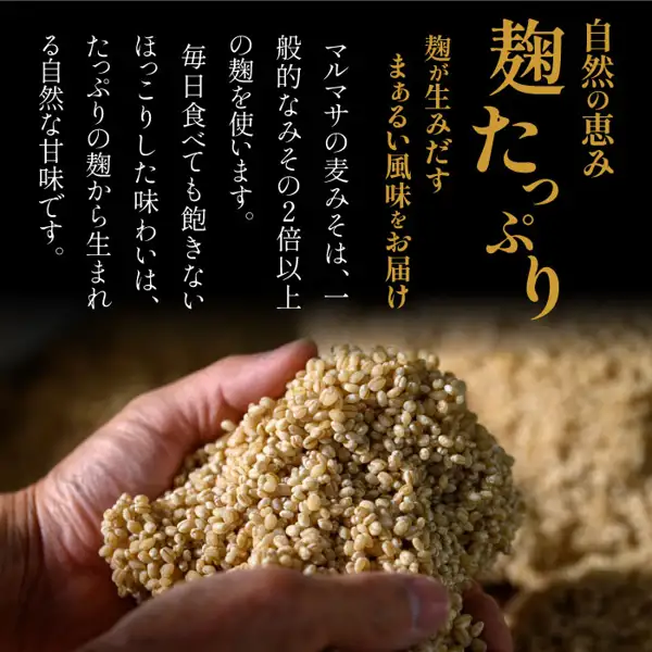 黒い背景の上に「自然の恵み」「麹たっぷり」「麹が生みだすまぁるい風味をお届け」と書かれ、その横に縦書きで「マルマサの麦みそは、一般的なみその2倍以上の麹を使います。毎日食べても飽きないほっこりした味わいは、たっぷりの麹から生まれる自然な甘味です。」と書かれ、下半分に手のひらいっぱいの粒状の麦をすくった写真がある（店舗が画像に入れた表示）。 麦みそや 麦味噌 甘口 500g×5（味噌の通販 麦みそや）