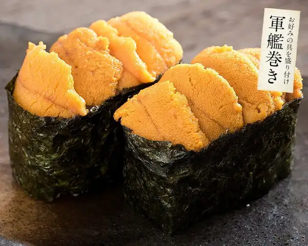Photo of a usage example for Minato Dining Shioso's wakeari roasted nori. Two gunkan-maki sushi made with roasted nori and sea urchin sit side by side on a dark brown plate (the sea urchin is not included with the product). Text the shop placed in the image reads “お好みの具を盛り付け” (top with your favorite fillings) and “軍艦巻き” (gunkan-maki) at the top right
