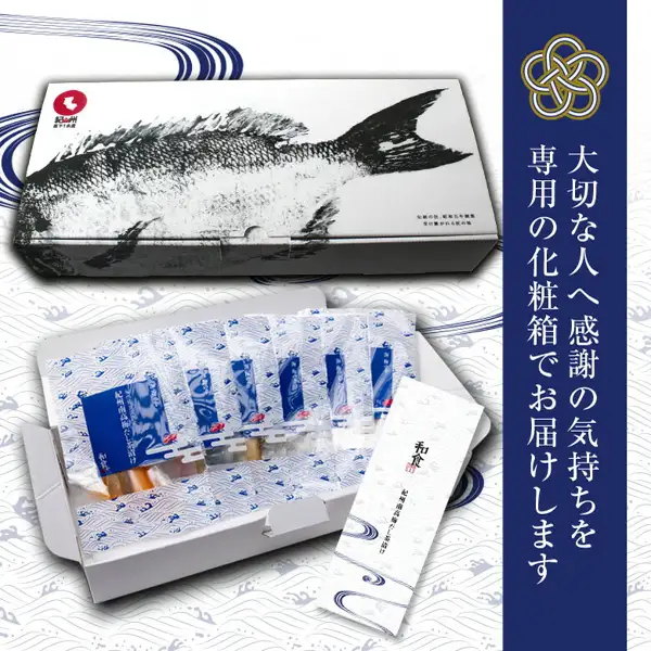 紀州備長炭熟成 紀州南高梅だし茶漬け 6種7食の化粧箱の写真。魚の拓本のような絵柄の白い化粧箱の下に、ふたを開けた箱の中の小袋の列と、「和食」と書かれた細長い紙が写る。箱に小さな印字があるが判読できない。画像内に店舗が画像に入れた表示として、「大切な人へ感謝の気持ちを専用の化粧箱でお届けします」「紀州南高梅だし茶漬け」「和食」の文字あり。