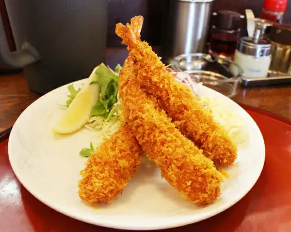 白い皿にエビフライを盛り、レモンと千切りキャベツ、細切りの野菜を添えた調理例の写真