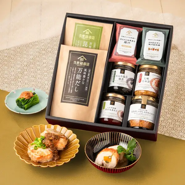 久世福商店 ごはんのお供(拌饭小菜)ギフト的8件商品装在黑色礼盒中的商品照片。礼盒前方摆着作为盛盘示例的2盘鸡肉料理和1小碟青菜。鸡肉、青菜和餐具均不包含在商品中。