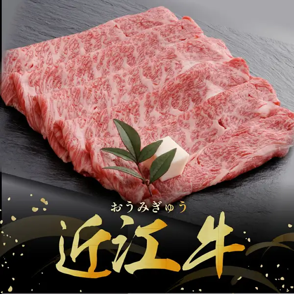 黒い石板の上に霜降りの牛肩ロースの薄切り肉を重ねて並べ、飾りの葉と白い飾りが添えられた商品写真（千成亭 近江牛 肩ロース スライス すき焼き用 500g）。店舗が画像に入れた表示として「おうみぎゅう」「近江牛」の文字