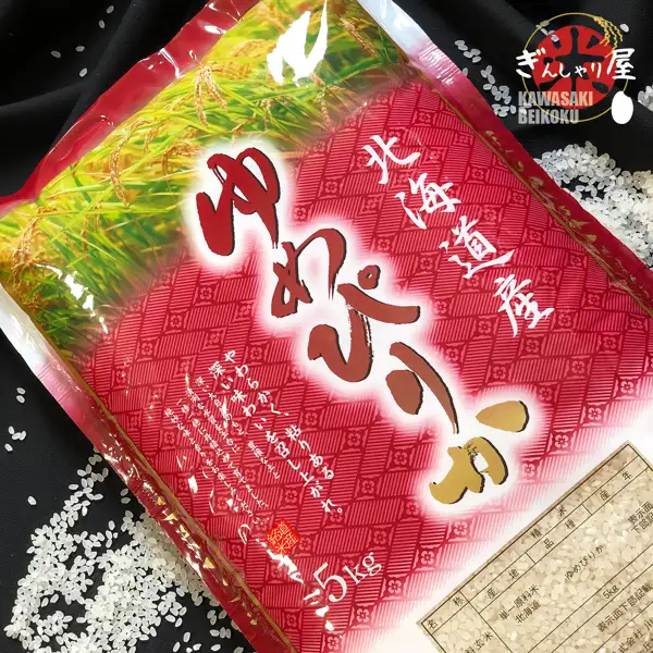 Product photo of a red bag of Hokkaido-grown Yumepirika 5kg rice laid diagonally on black cloth, with white rice scattered around it. The bag is printed with “北海道産” (Hokkaido-grown), “ゆめぴりか” (Yumepirika) and “5kg”, and the shop logo “ぎんしゃり屋 KAWASAKI BEIKOKU” is at the upper right