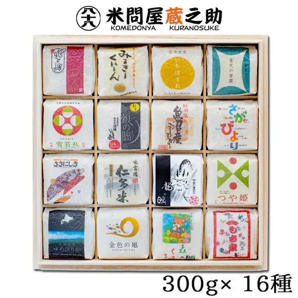 Product photo of the 米問屋蔵之助 Rice Gift Taste-Comparison Set, 2 go × 16 Varieties, in a Wooden Box. Sixteen small white bags, each with a different design, sit in a wooden box in four rows of four. Text added by the seller to the image: the shop logo “米問屋蔵之助 KOMEDONYA KURANOSUKE” at the top and “300g× 16種” at the bottom.