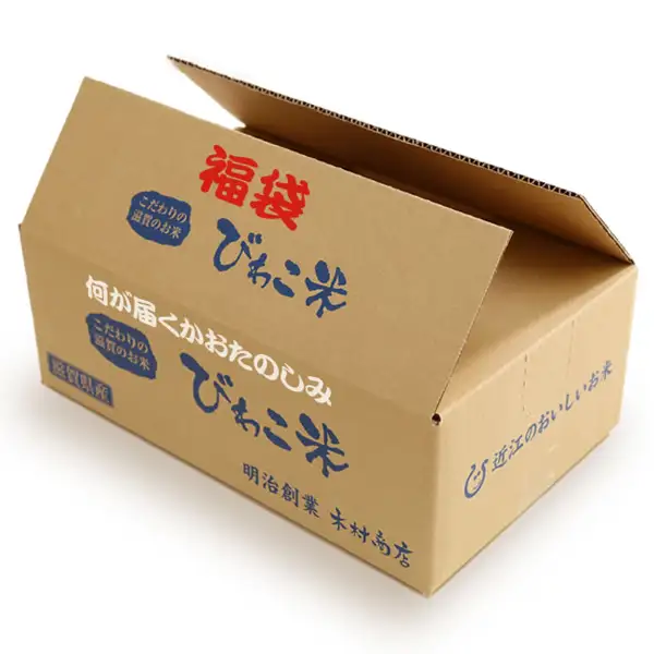 打开的纸箱商品照片。箱上有店铺自行加入的标示「福袋」「何が届くかおたのしみ」「こだわりの滋賀のお米」「びわこ米」「滋賀県産」「明治創業 木村商店」「近江のおいしいお米」。木村商店 滋贺县产 福袋(惊喜套餐)米 10kg的包装箱示例。