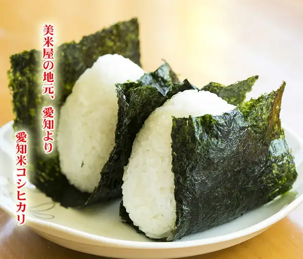 皿の上に、海苔を巻いた白いおにぎり2個を盛った愛知県産コシヒカリ（あだちねっと 美米屋）の店舗掲載写真。画像内に店舗が画像に入れた表示として、「美米屋の地元、愛知より」「愛知米コシヒカリ」の文字あり。