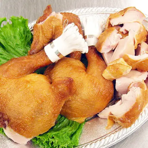サンライズファーム 烟熏烤鸡 整只：银色椭圆盘中摆放着套有白色纸饰的2根带骨鸡腿和切开的烟熏烤鸡肉块，并配有生菜的照片。这是切开后的摆盘示例，生菜不包含在商品内。商品本身是整只鸡，并非图中切开的状态