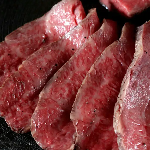 黒っぽい器の上に、赤い断面に白い脂が細かく入ったローストビーフの薄切りを重ねて並べた商品写真（豊代 A4・A5黒毛和牛 プレミアム ローストビーフ 約350g・とうがらし・特製ソース付）。画像内に文字はありません