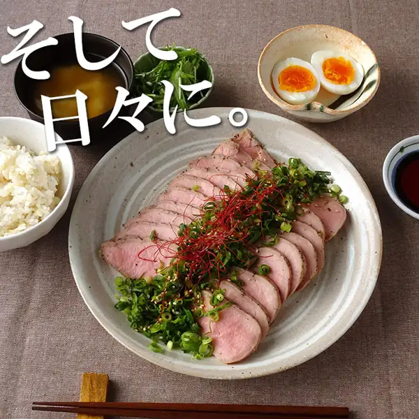 摆盘示例照片：陶制大盘中摆放着切成薄片的米久 豚ひれ肉のローストポーク（烤猪里脊，约360g），撒有葱花和辣椒丝，旁边配有米饭、味噌汤、半熟蛋和蘸酱（米饭、味噌汤、鸡蛋、葱、辣椒丝、蘸酱均不包含在商品中）。店铺添加在图片中的标示：「そして日々に。」（日常餐桌也适用）