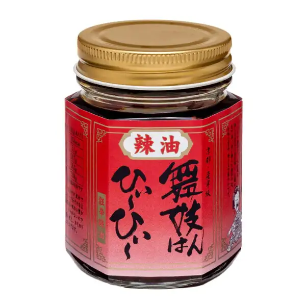 舞妓はんひぃ~ひぃ~セット(一味・七味・ラー油)のうち、ラー油の容器1点の商品写真。金属のねじ蓋をつけた角のある透明な瓶に赤いラベルが巻かれている。ラベルの印字「辣油」「舞妓はんひぃ~ひぃ~」「京都・産寧坂」。ラベルの両端には小さな印字とイラストがあるが、小さくて判読できない