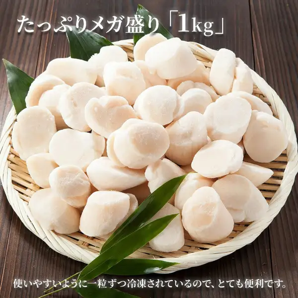 北海道产ほたて貝柱（扇贝柱）特A/A规格 1kg的商品照片。竹叶铺底的竹筐里堆满冷冻的白色扇贝柱。店铺放入图片的标示：「たっぷりメガ盛り「1kg」」「使いやすいように一粒ずつ冷凍されているので、とても便利です。」