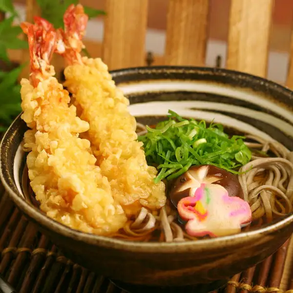 茶色の器に盛った温かいそばに、えび天2本・刻みねぎ・しいたけ・花形のかまぼこをのせた写真（本田商店 出雲だんだんそば 6人前）