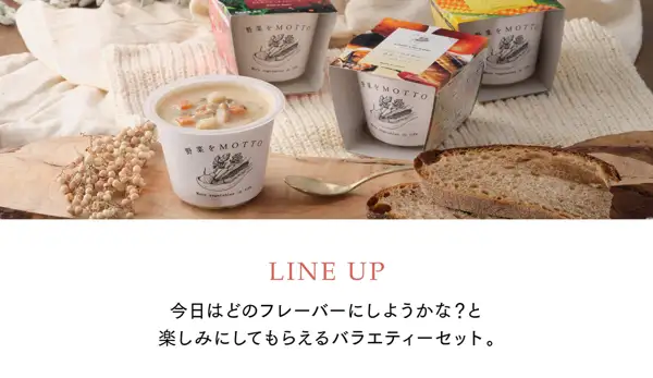 木板上摆放着一杯打开盖子的蛤蜊浓汤（可见胡萝卜、土豆等配料）、三个套着纸套的白色杯子、金色汤匙、切片面包和白色果实枝条的商品照片（野菜をMOTTO 国産野菜スープ おまかせ6個ギフトセット）。杯身印有“野菜をMOTTO”“More vegetables in life”，中间的纸套印有“Clam chowder”“あさりと国産野菜の濃厚クリーミーなクラムチャウダー”“Made in Japan”。店铺在图片中加入的标示：“LINE UP”“今日はどのフレーバーにしようかな？と楽しみにしてもらえるバラエティーセット。”