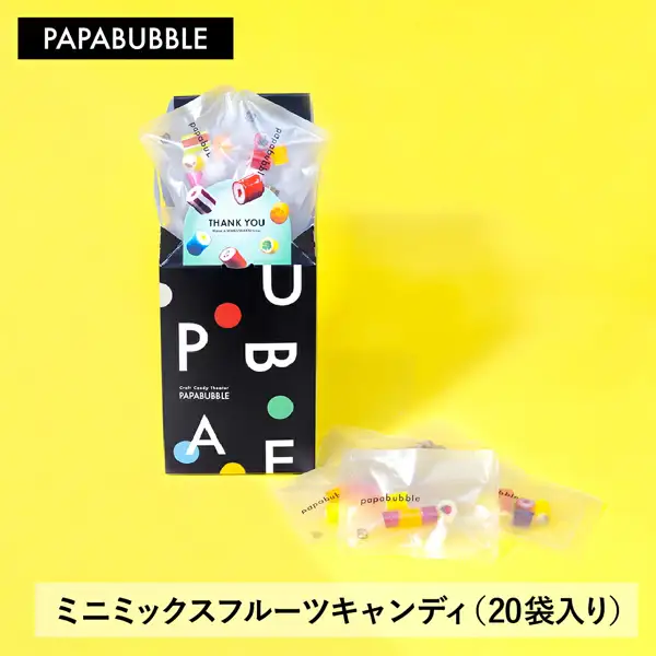 Product-page image of PAPABUBBLE Mini Mixed Fruit Candy, 20-bag set: against a yellow background, clear individually wrapped small bags come out of a black box, a card reading “THANK YOU” can be seen inside the box, and a few small bags lie in front. Text the shop put in the image: “PAPABUBBLE” at top left and “ミニミックスフルーツキャンディ（20袋入り）” (Mini Mixed Fruit Candy, 20 bags) at the bottom