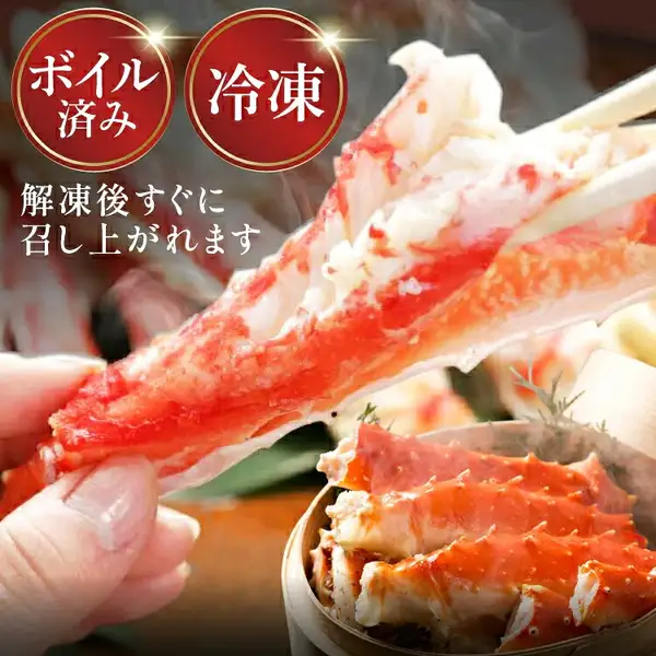 手に持ったボイル済みの冷凍タラバガニの脚の身を箸で示す商品写真（本タラバガニ脚 ボイル済）。奥の蒸籠にも脚が盛られている。画像内に店舗が画像に入れた表示として、「ボイル済み」「冷凍」「解凍後すぐに召し上がれます」の文字あり。