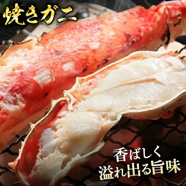 網の上で焼かれ、殻を開いて白い身が見えるタラバガニの脚の写真（本タラバガニ脚 ボイル済）。画像内に店舗が画像に入れた表示として、「焼きガニ」「香ばしく溢れ出る旨味」の文字あり。