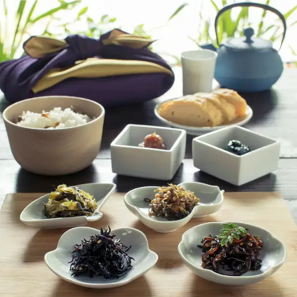 風呂敷包みと、小皿・小鉢に盛った佃煮6品、ご飯、だし巻き卵、急須が並ぶ盛り付け例の写真（おすすめ佃煮詰め合わせ 高菜 昆布 ひじき 青のりわかめ）。ご飯・だし巻き卵・急須は商品に含まれません