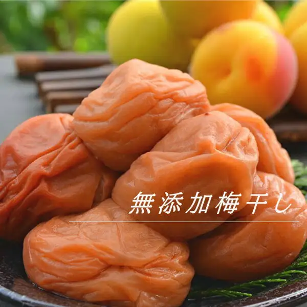 Photo of wrinkled, glossy orange-pink umeboshi piled together with ripe yellow-and-blush ume fruit behind them (Mutenka Umeboshi 600g, 古道の梅屋). Text the shop added to the image: “無添加梅干し”