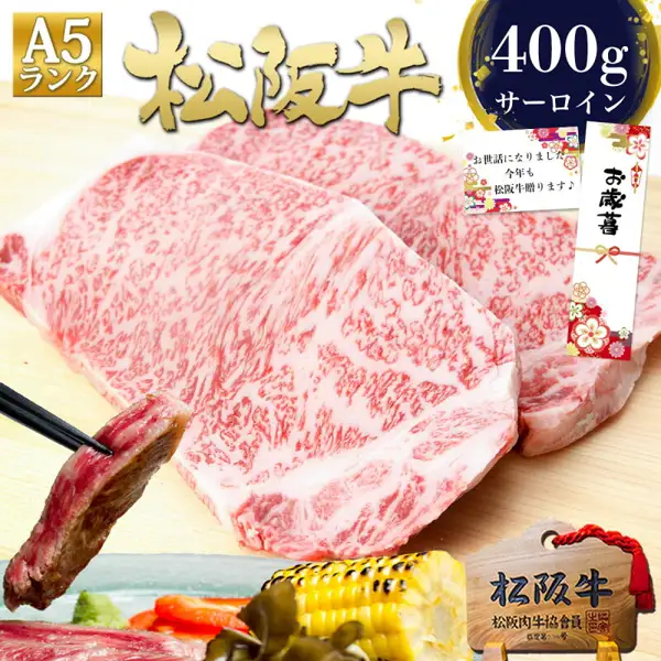 松阪牛 A5 サーロインステーキ 200g×2枚の商品写真（盛り付け例）。木の板の上に生のサーロインステーキ肉2枚が並び、左下には焼いた肉を箸でつまむ様子、手前にはとうもろこし、わさび、赤いパプリカ、海藻のようなものが添えられている。店舗が画像に入れた表示として「A5ランク」「松阪牛」「400g サーロイン」、のし風の「お歳暮」の札、「お世話になりました 今年も松阪牛贈ります♪」と書かれたメッセージカード風の札、「松阪牛 松阪肉牛協会員」と書かれた木札がある。