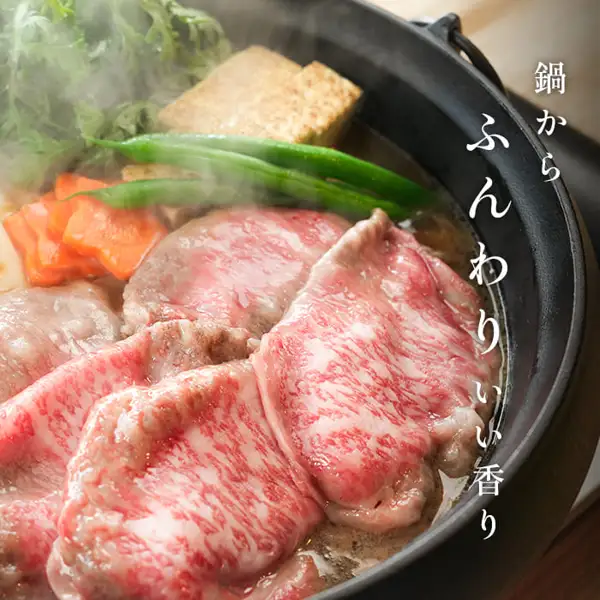 肉処 三代目本多 国産黒毛和牛 メガ盛肩ロースすき焼きスライス 1kgの盛り付け例の写真。黒い鉄鍋で牛肩ロースのスライスを焼き豆腐・にんじん・緑の野菜と一緒に煮ている様子で、店舗が画像に入れた表示「鍋からふんわりいい香り」。焼き豆腐・にんじん・緑の野菜は商品に含まれない