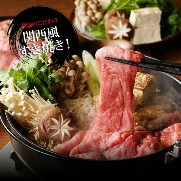 黑色铁锅中用长筷夹起薄切牛肉，与金针菇、蟹味菇、香菇、豆腐、青菜、葱一起煮制的寿喜烧摆盘示例照片（うし源本店 大和榛原牛 シンタマスライス すき焼き用 800g）。店铺自行加入图片的文字为“老舗のこだわり 関西風すき焼き！”（老字号的讲究 关西风寿喜烧！）。菌菇、豆腐、青菜、葱不包含在商品中