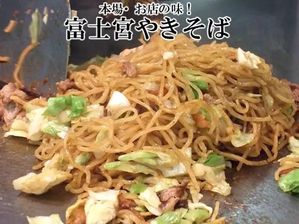 在铁板上与卷心菜和肉一起炒制的富士宮炒面烹调示例照片（特選 富士宮やきそば 10人前セット）。店铺在图片上方加入的文字：「本場・お店の味！」「富士宮やきそば」。